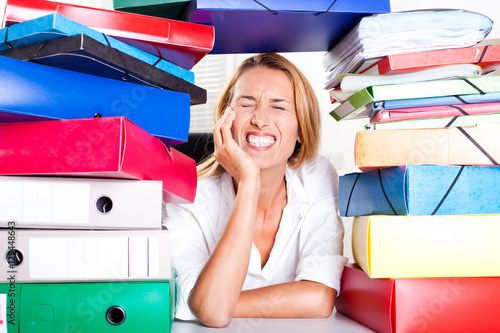 femme au bureau qui fait la grimace sous une pile de dossiers photo