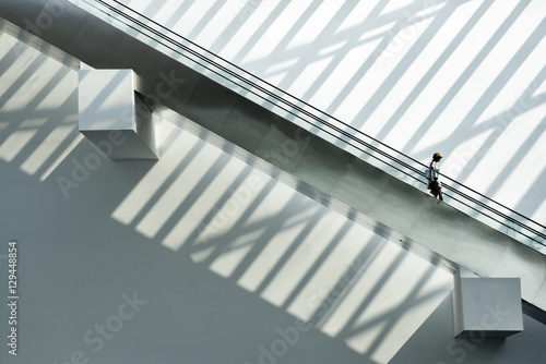 Lonely person on moving stairs in a shopping mall in futuristic light and shadow architecture photo
