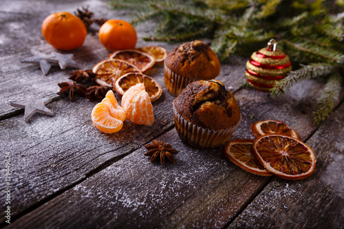 Xmas or new year composition with holiday decoration - Homemade cupcakes, sliced dried oranges and mandarin on wooden background with spruce twigs and christmas toy. Xmas card. Space for text