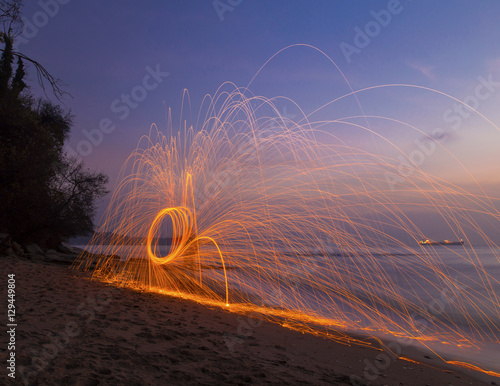 Man twirling fireworks on beach at sunrise