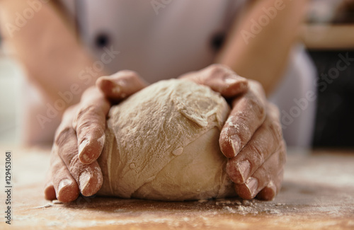 Close-up of chef hands kneading raw bread dough on wooden board.