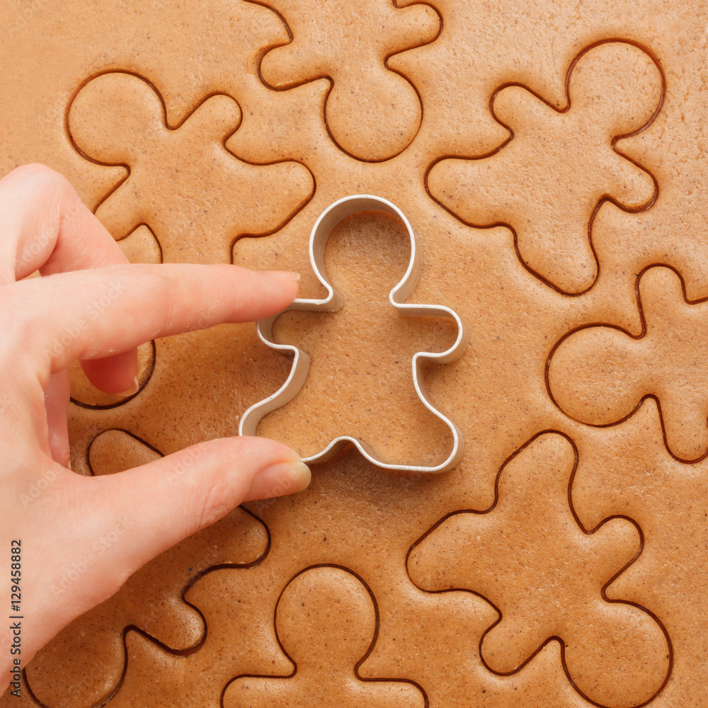 Closeup of female hand with cutter making homemade traditional gingerbread men Christmas cookies. Above view Closeup of female hand with cutter making homemade traditional gingerbread men Christmas cookies. Above view
