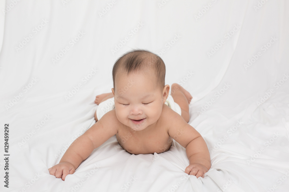 smiling surprised baby lying on a white bed. Baby born in Thailand, Asia. Infants aged 5 months smiling surprised baby lying on a white bed. Baby born in Thailand, Asia. Infants aged 5 months