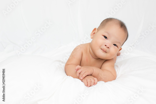 smiling surprised baby lying on a white bed.  Baby born in Thailand, Asia.  Infants aged 5 months
