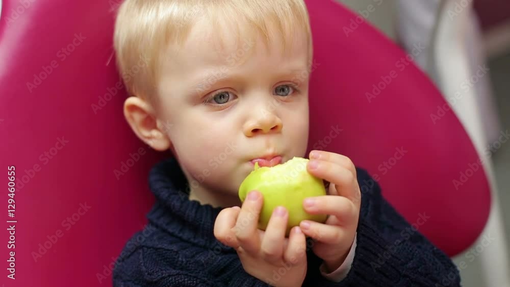 Little boy eats an apple in the dental clinic. The child sits in the dental chair with an apple. Children dentistry. Little boy eats an apple in the dental clinic. The child sits in the dental chair with an apple. Children dentistry.