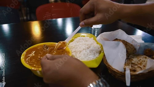 Hands mix butter chicken with steamed basmati rice
