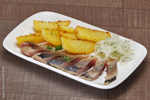 Fototapeta Naklejka Na Ścianę i Meble -  Plate of pieces of herring with fried potato and pickled onion.