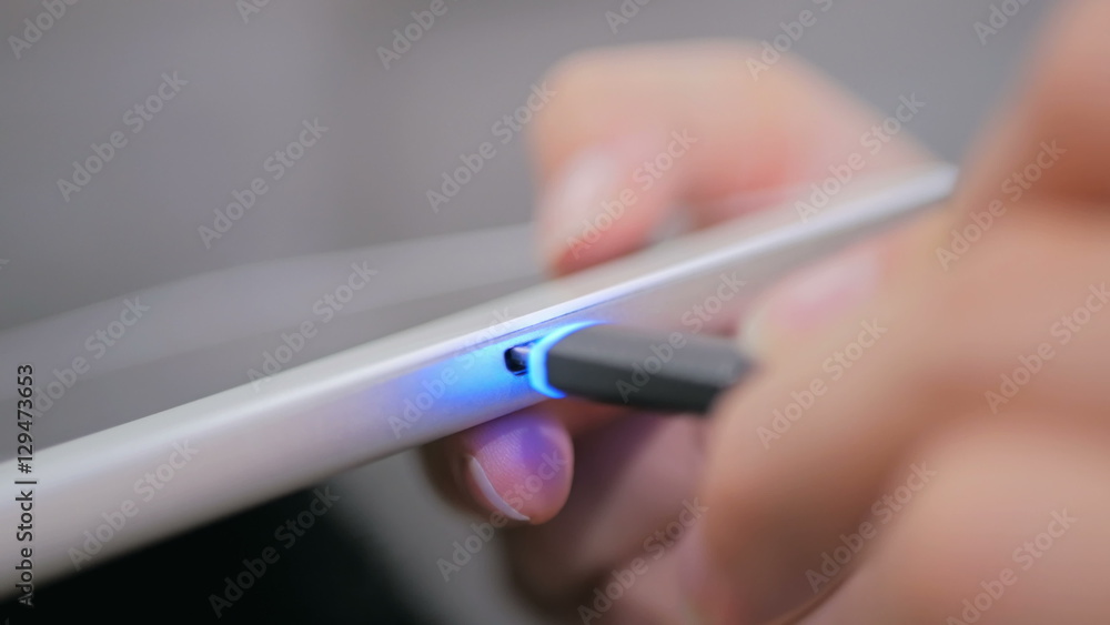 Woman's hand plugging black lightning charging cable into pc digital tablet - USB data cable connecting on modern gadget. Close up Woman's hand plugging black lightning charging cable into pc digital tablet - USB data cable connecting on modern gadget. Close up