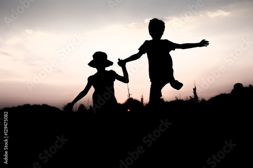 Silhouettes Of Kids Jumping Off A Cliff At Sunset Boy And Girl Jump High Holding Hands Brother And Sister Having Fun In Summer Friendship Freedom Concept Twins On Vacation In Mountains Stock