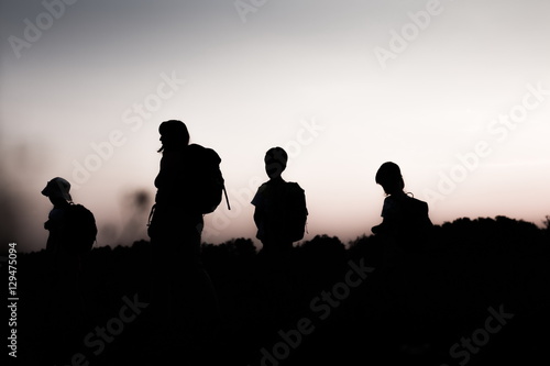 Silhouette of family hiking at sunset. Happy big family on summer vacation in mountains. Mother and kids carry backpacks. Tourists walking on cliff edge.Summertime.Little children traveling.