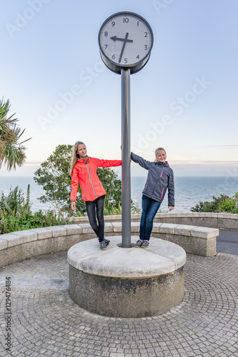 2 Mädchen posieren an der julianischen Uhr in Folkestone mit Darstellung der Uhrzeit in dezimalen Unterteilungen photo