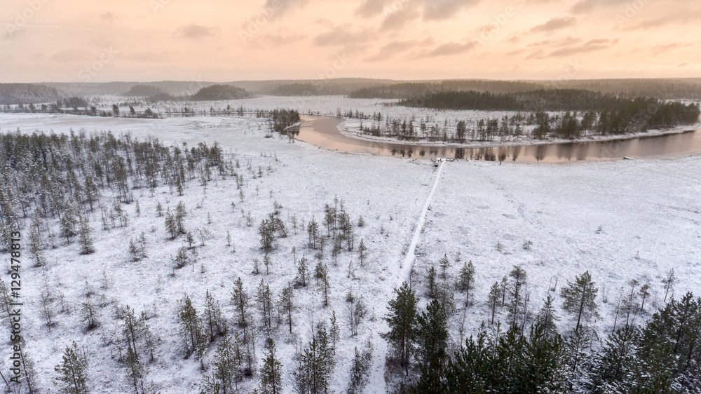 Wintry river with open water and snow covered shores. Sunset sun light is on horizon. Karelia, Russia