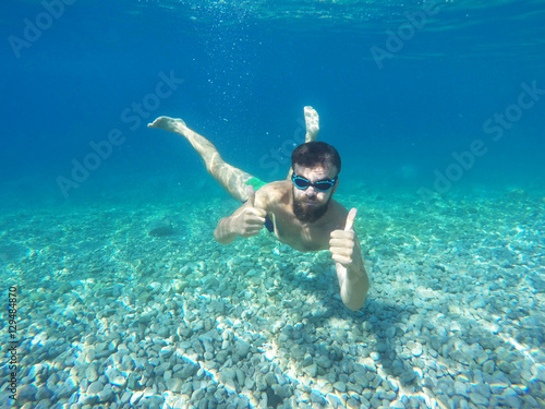 Beard man with glasses diving in a blue clean water with thumb u