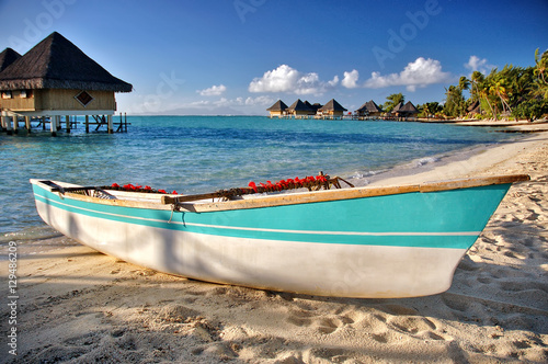Boat on Bora Bora beach with blue ocean, bungalows background