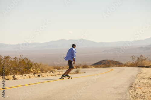 A man skateboarding down a desert highway through Joshua Tree National Park, California.