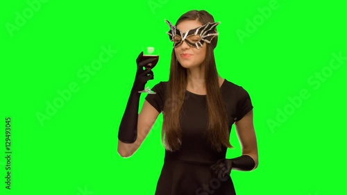 The girl in the mask and black dress drink wine. and enjoys