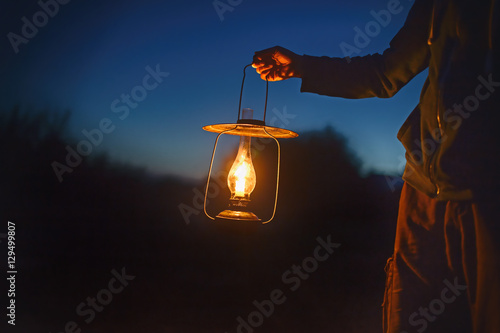 man holding the old lamp with a candle outdoors. hand holds a large lamp in the dark. ancient lantern with a candle illuminates the way on a night photo