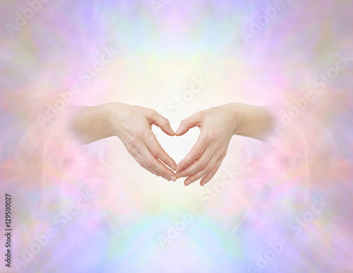 Sacred heart hand sign - female hands with thumbs and fingers touching making a heart shape on an ethereal heavenly angelic background