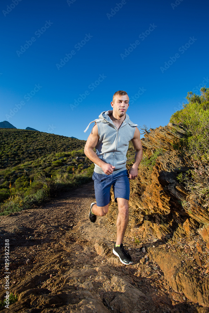 Naklejka premium Male cross country athlete running in the hills on a warm and su