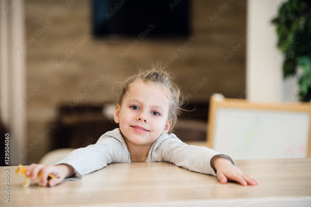 Naklejka premium Beautiful calm little girl sitting at wooden table