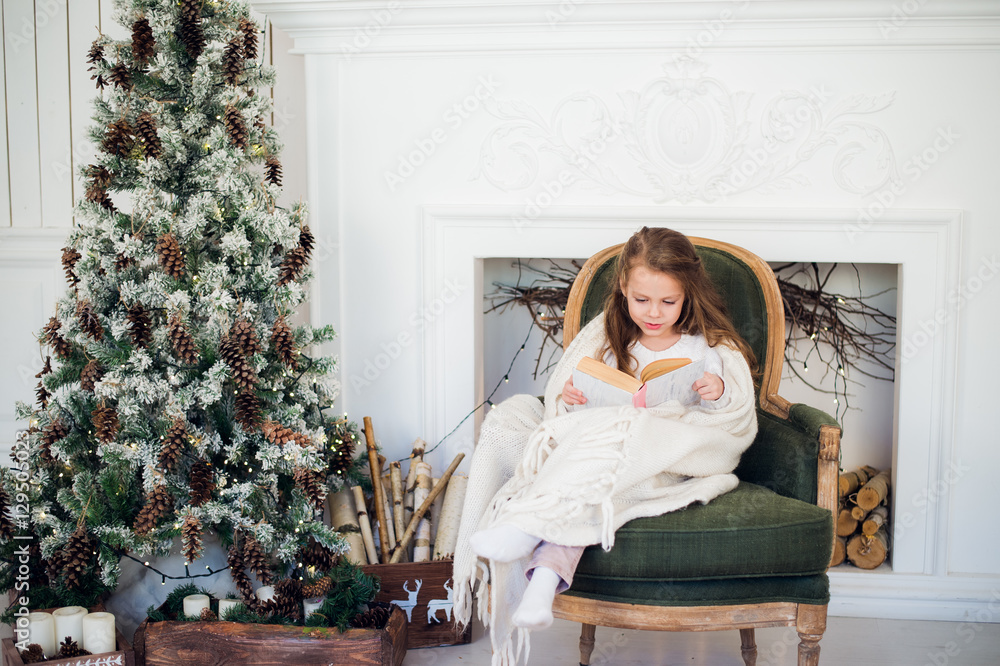 Little girl reading book near Christmas tree