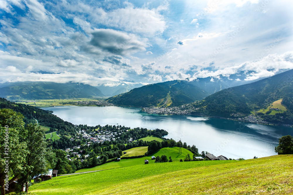 View over Zeller See lake. Zell Am See, Austria, Europe. Beautiful green meadows and pines at foreground, Alps at background. View over Zeller See lake. Zell Am See, Austria, Europe. Beautiful green meadows and pines at foreground, Alps at background.