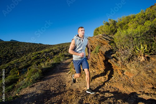 Male cross country athlete running in the hills on a warm and su