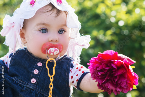 cute little baby girl looking on the flower in her hand. child with big blue eyes in a summer hat on the nature, outdoor