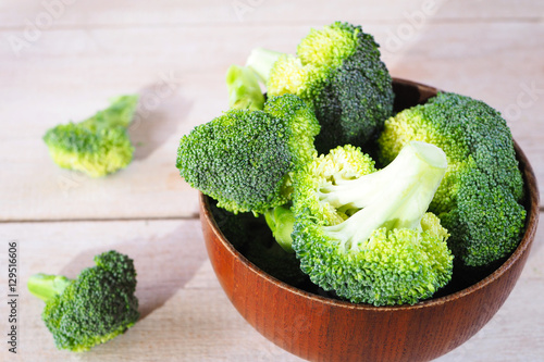 Close up of fresh green broccoli in a wooden bowl on a wooden background.