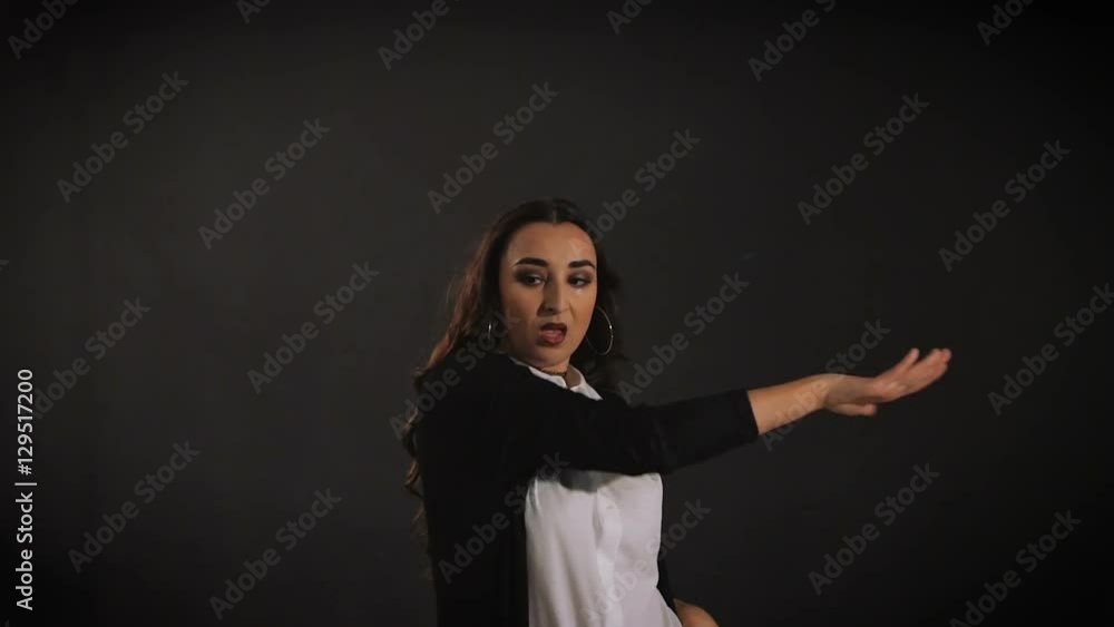 Stylish long-haired young woman in white shirt and black jacket is performing modern jazz dancing with her hands and body with black wall in the background. Stylish long-haired young woman in white shirt and black jacket is performing modern jazz dancing with her hands and body with black wall in the background.