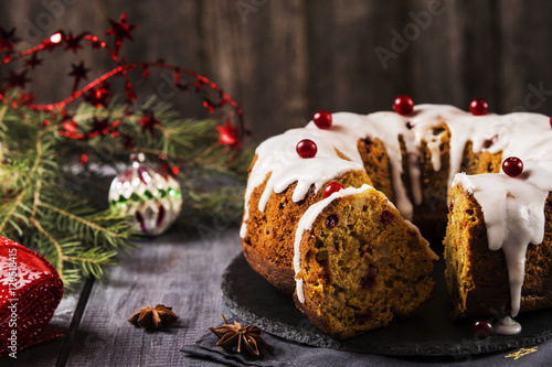 Christmas homemade cake with nuts, apples and cranberries with icing on dark wooden background. Selective focus 