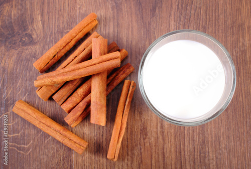 Fragrant cinnamon sticks and glass of milk on wooden surface