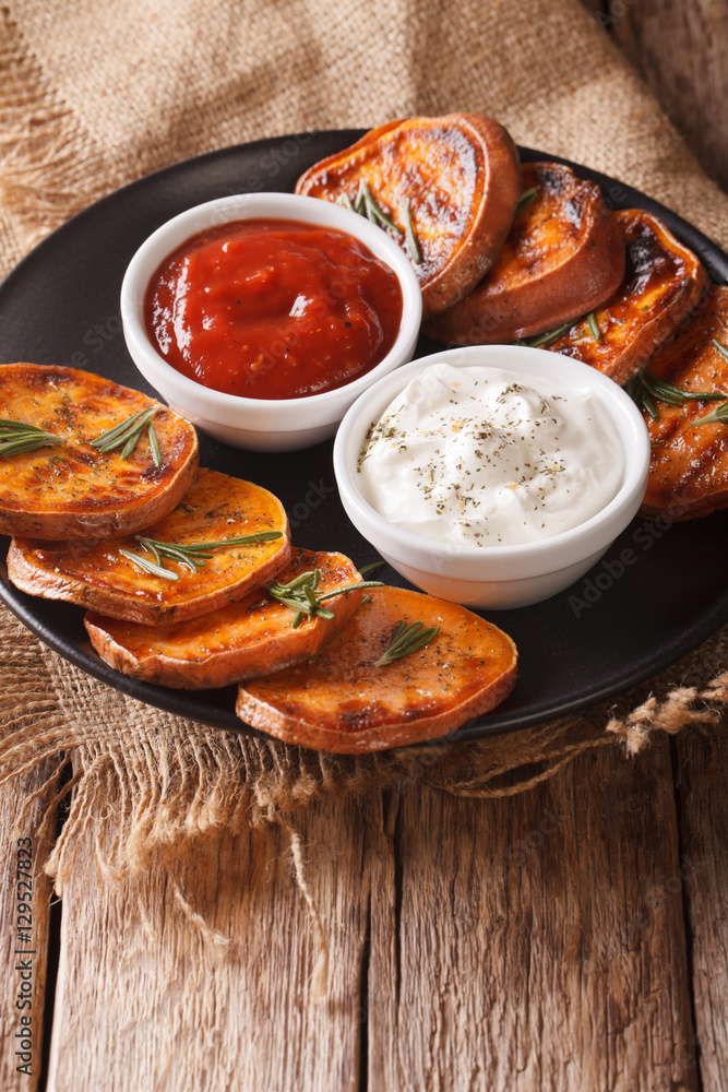 roasted sweet potatoes with rosemary served with sour cream and ketchup closeup. vertical