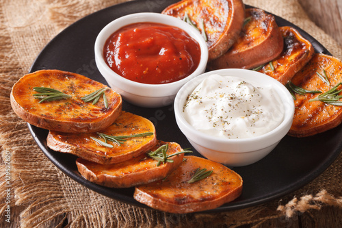 roasted sweet potatoes with rosemary served with sour cream and ketchup closeup. Horizontal