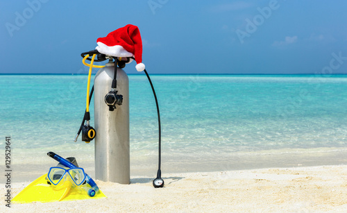 Taucherflasche und Schwimmflossen mit Weihnachtsmütze am tropischen Strand