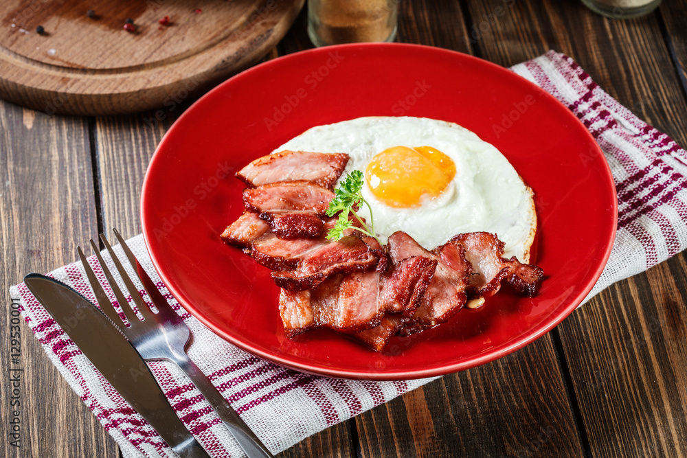Slices of smoked bacon and fried egg on a red plate Slices of smoked bacon and fried egg on a red plate