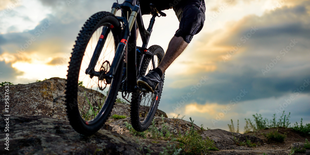 Obraz premium Professional Cyclist Riding the Bike Down Rocky Hill at Sunset. Extreme Sport. Space for Text.