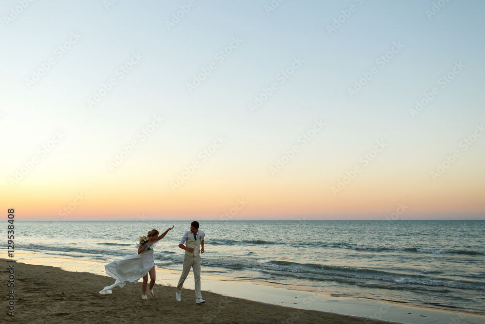 Laughing bride and groom run along the shore in evening lights Laughing bride and groom run along the shore in evening lights