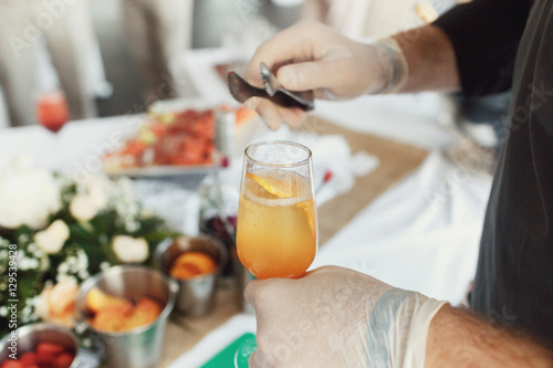 Man puts slices of fruits in glass with champagne