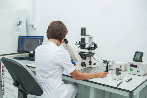 Young woman medical researcher looking through microscop slide in the life science (forensics, microbiology, biochemistry, genetics, oncology) laboratory. Medicine concept.