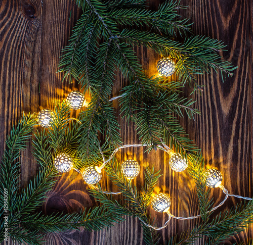 square christmas background with string lights and fir branches on wooden planks.