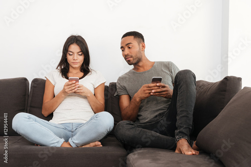 Couple using cellphones sitting on sofa at home
