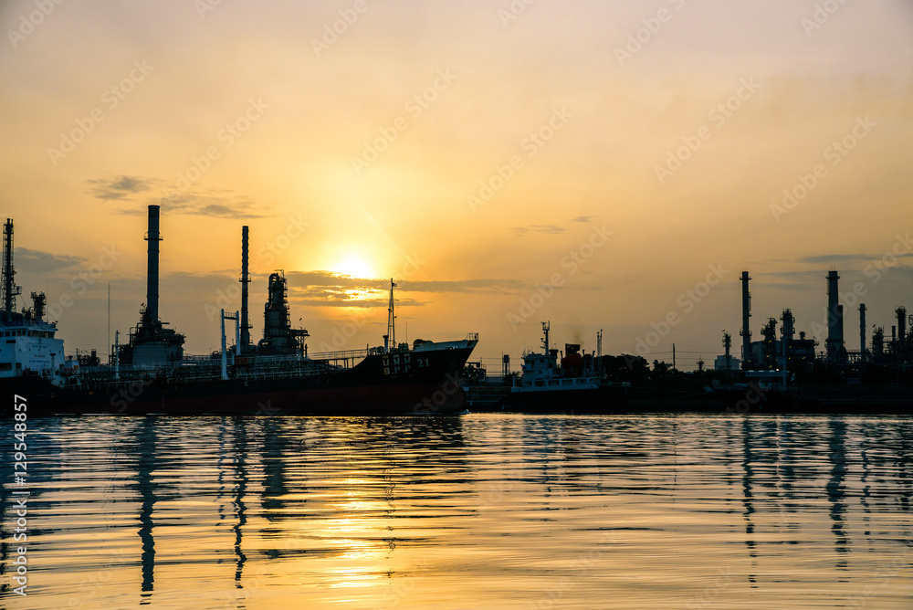 Big gold sun over the oil refinery in silhouette.