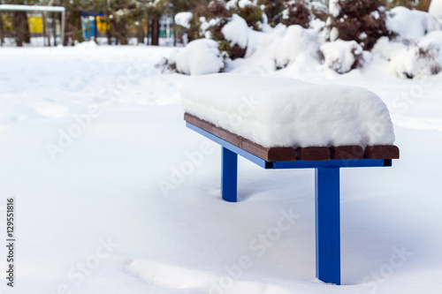 Wooden bench covered by snow in winter day.