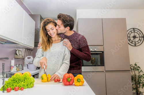 Happy beatiful young couple have fun in modern kitchen indoor while preparing fresh vegetables food salad