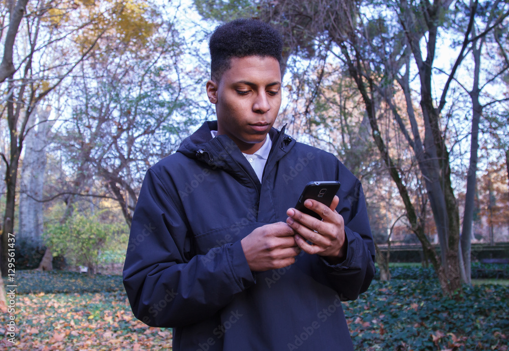 Black man sending messages with his smartphone in the field. Black man sending messages with his smartphone in the field.