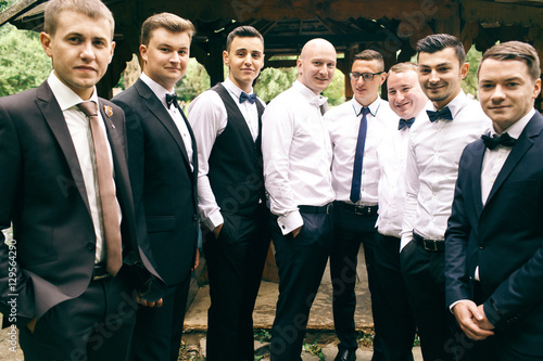 Grom and groomsmen stand on the backyard holding their hands in