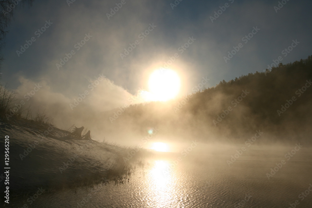 Winter landscape. Foggy winter sunset, colorful winter evening, bright sunshine over a river Winter landscape. Foggy winter sunset, colorful winter evening, bright sunshine over a river