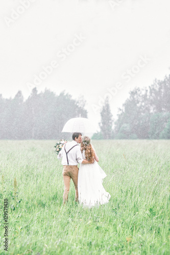 The bride and groom are on the field. The young couple got caught in the rain.