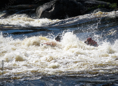 Men on an inflatable catamaran overcome the threshold of the turbulent river. Catamaran is not visible. 